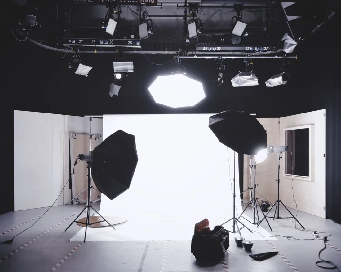 Fotoateliér s bílým pozadím, dvěma softboxy na stativech a závěsnou světelnou rampou pod stropem